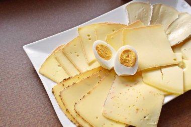 Farklı peynir türleriyle dolu beyaz bir tabak. Almanya 'da akşam yemeği için beyaz bir tabakta dilimlenmiş peynir.