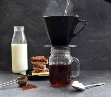 Fındık köşeleri, şeker ve süt dolu koyu bir arka plana karşı filtre torbasından taze buğulanmış kahve.