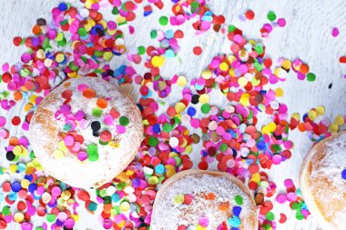 Almanya 'dan gelen karnaval çörekleri, üzerinde konfeti ve flamalar olan hafif ahşap bir yüzeyde krema şekeri ile bir karnaval partisi ya da partiler için arka plan.