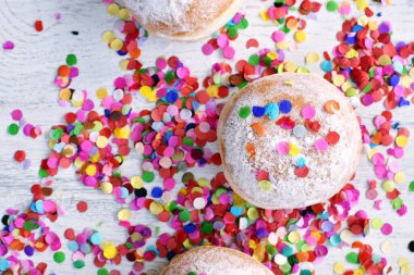 Almanya 'dan gelen karnaval çörekleri, üzerinde konfeti ve flamalar olan hafif ahşap bir yüzeyde krema şekeri ile bir karnaval partisi ya da partiler için arka plan.