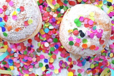 Almanya 'dan gelen karnaval çörekleri, üzerinde konfeti ve flamalar olan hafif ahşap bir yüzeyde krema şekeri ile bir karnaval partisi ya da partiler için arka plan.