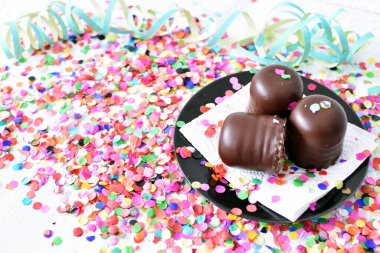 Çikolata kaplı küçük kremalı pastalar konfeti ve flamalarla bir yüzeyde dururlar. Çikolata marşmelovu parlak bir yüzeyde karnaval için dururlar.