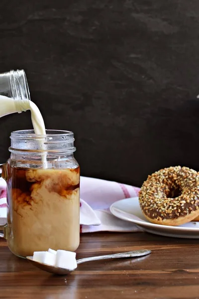Fındık köşeli koyu bir arka fona karşı kahve dolu bir bardağa süt dökün - taze demlenmiş sıcak kahve içine süt akan koyu bir ayara karşı.