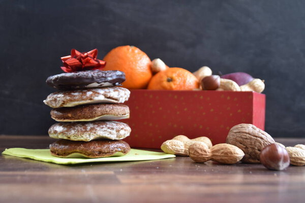 On a bright wooden surface are various types of nuts next to a few delicious German Elisenlebkuchen - German gingerbread on a base as a background