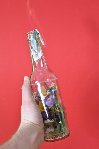 Molotov cocktail filled with colorful flowers - loving resistance depicted over a burning surface filled with flowers - abstract eco-fighting