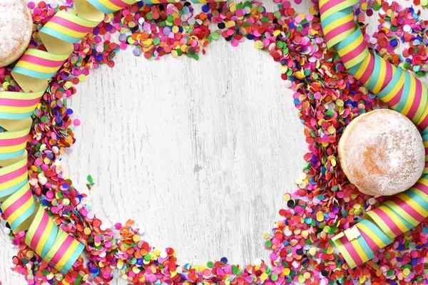 Almanya 'dan gelen karnaval çörekleri, üzerinde konfeti ve flamalar olan hafif ahşap bir yüzeyde krema şekeri ile bir karnaval partisi ya da partiler için arka plan.