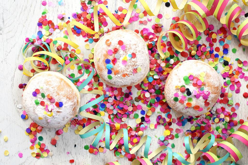 Carnival donuts from Germany with icing sugar on a light wooden surface with confetti and streamers on it - background for a carnival party or parties