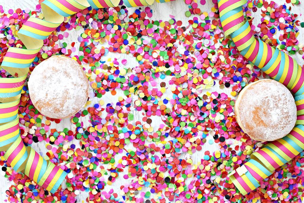 Carnival donuts from Germany with icing sugar on a light wooden surface with confetti and streamers on it - background for a carnival party or parties