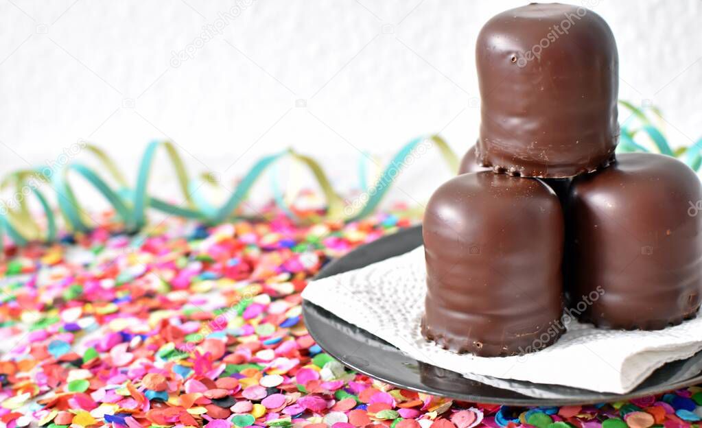 small chocolate-covered cream cakes stand on a surface with confetti and streamers - chocolate marshmallow stand for carnival on a bright surface