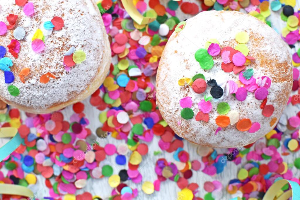 Carnival donuts from Germany with icing sugar on a light wooden surface with confetti and streamers on it - background for a carnival party or parties