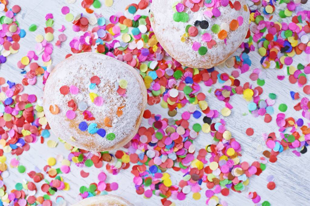 Carnival donuts from Germany with icing sugar on a light wooden surface with confetti and streamers on it - background for a carnival party or parties