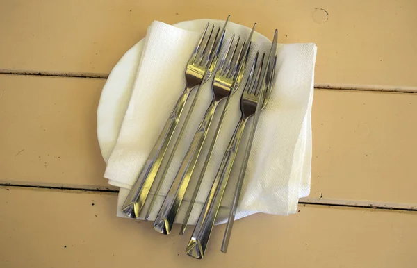 Sur une table en bois une assiette. Sur l'assiette se trouvent des fourchettes à couverts et des couteaux . — Photo