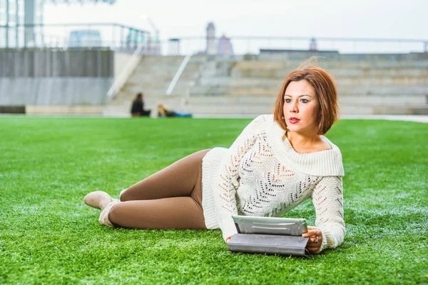 Young American Woman relaxing on green lawn in New York, reading tablet computer. — Stock Photo, Image