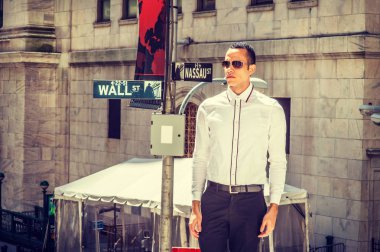Genç Amerikan seyahat, New York'ta çalışma, giydiği beyaz gömlek, siyah pantolon, güneş gözlüğü, güneş altında sokakta duran dört gözle iş adamı. Arka plan Wall Street işareti. Filtre uygulanmış etkisi