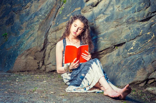 Young American Woman reading red book, sitting on ground, travel