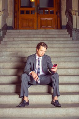 Merdivenlerde oturan cep telefonuyla Amerikalı işadamı manifatura