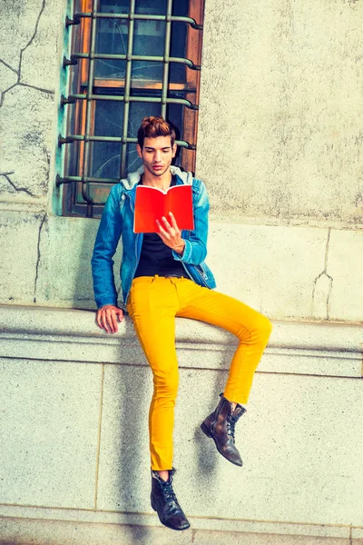 Молодой человек читает красную книгу, сидит на улице — стоковое фото