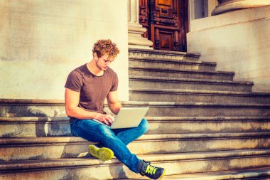 Genç dışında merdivenlerde oturan dizüstü bilgisayarda çalışan adam 