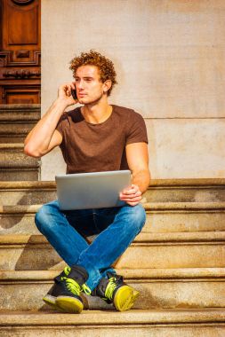 Genç dizüstü bilgisayar üzerinde çalışan erkeğin oturup cep telefonundan sohbet,