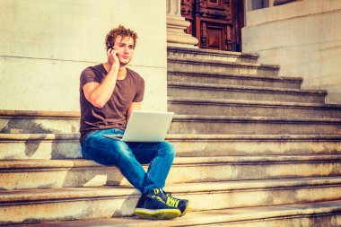 Genç dizüstü bilgisayar üzerinde çalışan erkeğin oturup cep telefonundan sohbet,