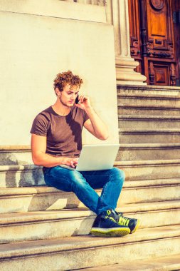 Genç dizüstü bilgisayar üzerinde çalışan erkeğin oturup cep telefonundan sohbet,