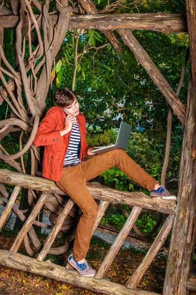 Genç dizüstü bilgisayar üzerinde çalışan C cep telefonuyla konuşan adam