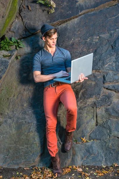 Genç adam kayalar tarafından dışında dizüstü bilgisayarda çalışma