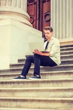 Genç Amerikalı adam az sakal okuyan, New York, giyen bej ceket, siyah pantolon, rahat ayakkabı çalışma, vintage office kapı aralığında merdivenlerde oturan, okuma, dizüstü bilgisayar üzerinde çalışan