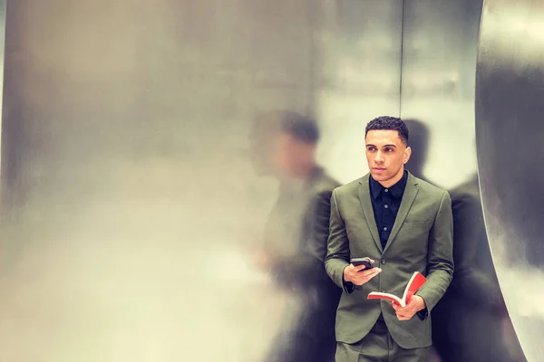 Joven hombre de negocios americano leyendo libro, mensajes de texto en el teléfono celular . — Foto de Stock