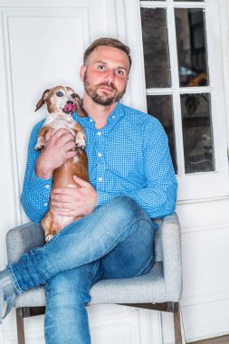 Sakallı, mavi desenli gömlek giyen, kot giyen, New York 'ta sandalyede oturan, bacak bacak bacak üstüne atan, Dachshund köpeği tutan, rahatlatan genç bir Amerikalı. En iyi arkadaşı olan bir adamın portresi.