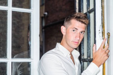 New York 'ta genç ve yakışıklı bir adamın portresi. 20 yaşında, uzun kollu beyaz gömlek giyen, pencerenin yanında duran, açık çerçeveyi tutan, ilginç bir şekilde sana bakan bir adam.