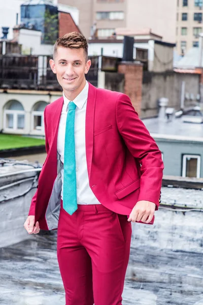 Little raining, drizzle, wet feel. 20 years old man with short hair, wearing red suit, white shirt, light green tie, standing on roof top outside in New York City, smiling. Portrait of Young Man