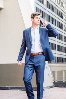 Genç Amerikan Koleji öğrencisi, New York 'ta çalışıyor, mavi takım elbise giyiyor, beyaz gömlek giyiyor, dizüstü bilgisayarı tutuyor, cep telefonuyla konuşuyor, kampüsün dışındaki balkonda yürüyor.