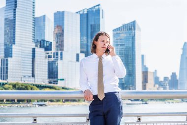 Uzun saçlı, cep telefonuyla konuşan, New York 'ta gezen, beyaz takım elbiseli, mavi pantolonlu, kravatlı, Manhattan' ın göbeğinde yüksek binaları olan genç bir Amerikalı.