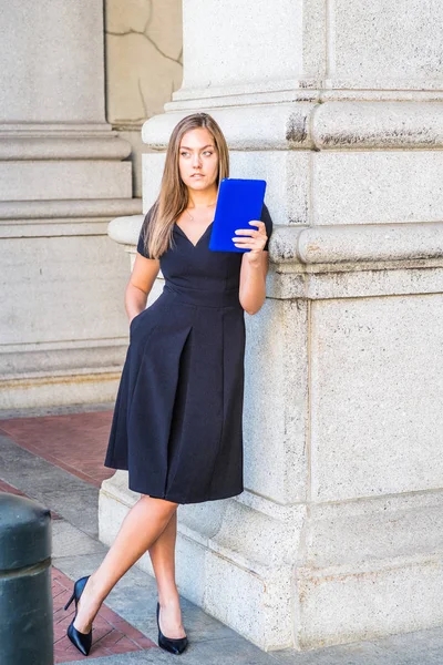 長い髪を持つ若い東ヨーロッパの女性 ニューヨーク市の外に青のタブレットコンピュータを読んで 黒の半袖を身に着けています Vネックドレス ハイヒール ヴィンテージ通りの列のそばに立って リラックス — ストック写真