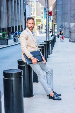 Genç Avrupalı iş adamı seyahat ediyor, New York 'ta çalışıyor, sakallı, küçük gri saçlı, bej ceketli, gri pantolonlu, deri sahilli, evrak çantalı, eski sokakta oturuyor, bekliyor, düşünüyor.