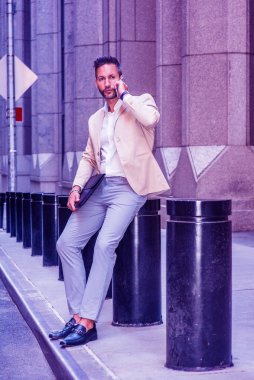 Renkli filtreli efekt. Avrupalı iş adamı seyahat ediyor, New York 'ta çalışıyor, sakallı, bej ceketli, gri pantolonlu, deri ayakkabılı, evrak çantalı, sokakta oturuyor, cep telefonuyla konuşuyor.