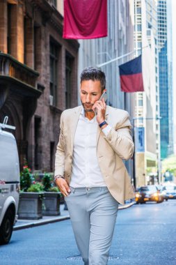Sakal, küçük gri saçlı Genç Avrupa New York, cep telefonuyla konuşurken Manhattan, yüksek binalar ile dar sokakta yürürken bej ceket, gri pantolon, beyaz gömlek giymiş seyahat adam