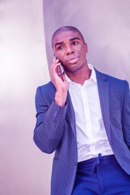 Kısa saçlı, New York 'un dışında cep telefonuyla konuşan, mavi ceketli, beyaz gömlekli, gümüş metal arka planda duran genç bir Afro-Amerikan iş adamı. Renkli filtrelenmiş efekt
