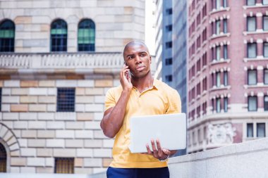 Herhangi bir yerde. New York 'ta çalışan, sarı kısa kollu gömlekli, ofis binasının dışında yürüyen, cep telefonuyla konuşan, dizüstü bilgisayarla çalışan genç bir Afro-Amerikan iş adamı.
