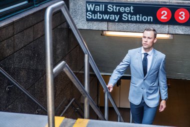 New York 'ta seyahat eden genç Avrupalı iş adamı gri ceket, beyaz gömlek, siyah kravat, merdivenlerde yürümek, parmaklıklara dokunmak, Wall Street metro istasyonundan dışarı çıkmak.