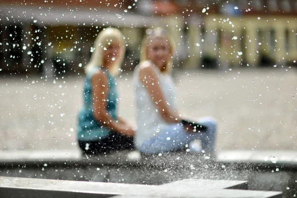 ДОБЕЛЬ, Латвия - 4 августа 2016 года: Абстрактный городской пейзаж. За фонтаном капли воды видны неизвестные женские силуэты . — стоковое фото