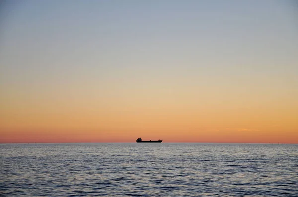 Sea at sunset far away can be seen the silhouette of the ship. — Stock Photo, Image