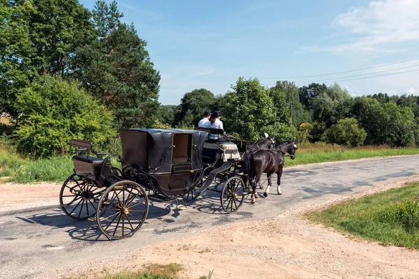 By the way leaves wedding carriage with two horses.