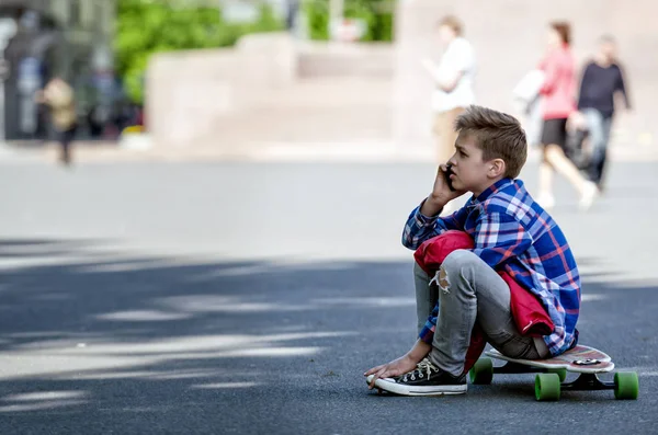 The boy sits on a skateboard and talk on the telephone. — Stock Photo, Image