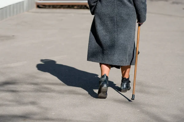 В солнечный день пожилая женщина идет по улице с тростью. Тень женщины видна на тротуаре. Вид сзади . — стоковое фото