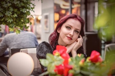 Retro moda giysilerle açık bir kafede oturan genç güzel kızıl saçlı kadın giyinmiş.