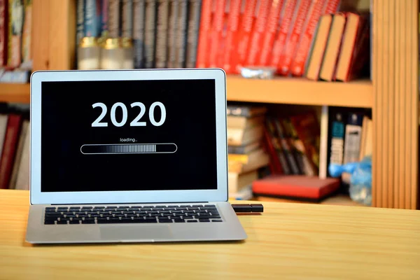 На столе ноутбук с текстом - 2020 загрузки - на экране, размытые полки с книгами в фоновом режиме — стоковое фото