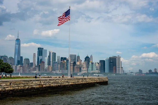 New york, usa - 7. Juni 2019: amerikanische Flagge auf der Freiheitsinsel im New Yorker Hafen und der Skyline von Manhattan - image — Stockfoto