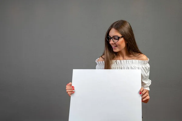 Beautiful woman holding a blank billboard isolated on gray background. — Stock Photo, Image